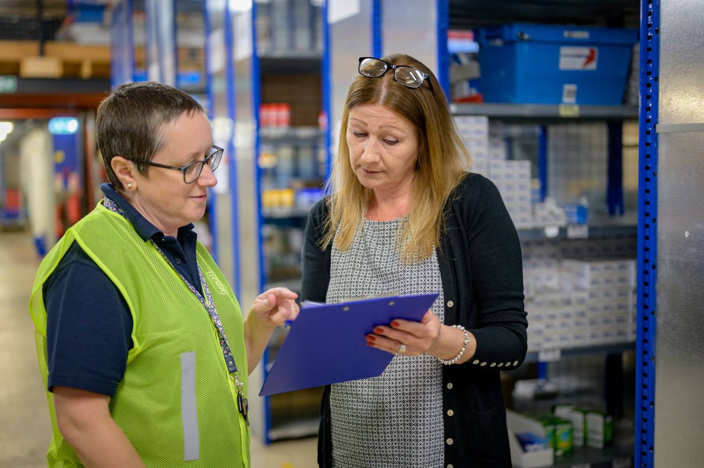 Two warehouse coordinators reviewing inventory on a clipboard.
