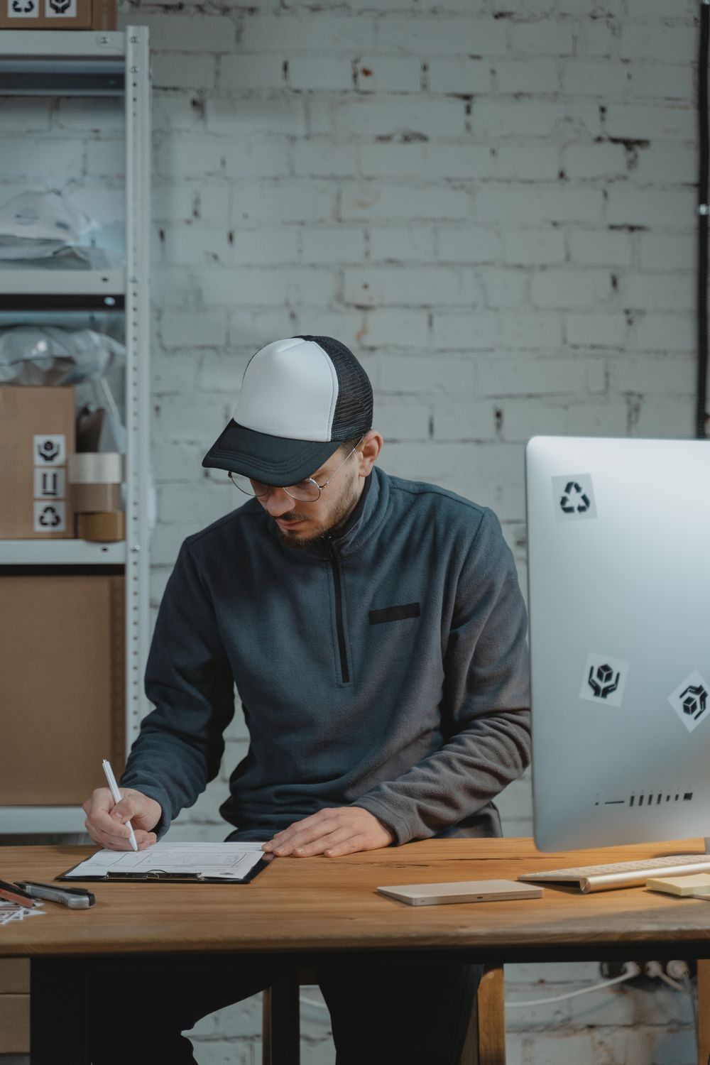 Employee completing paperwork at a desk beside warehouse shelving.